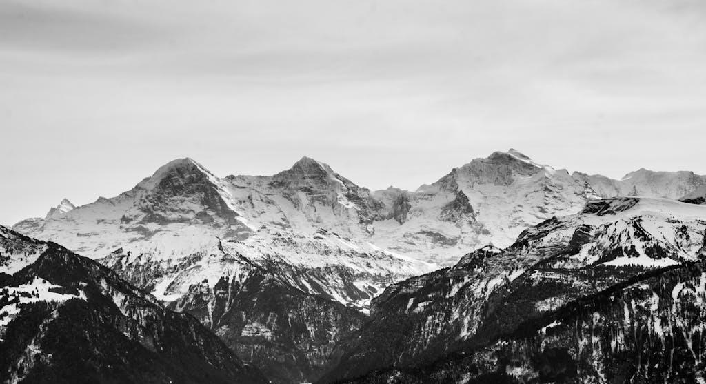 Black and white photo capturing majestic, snow-capped mountains in a serene winter landscape.
